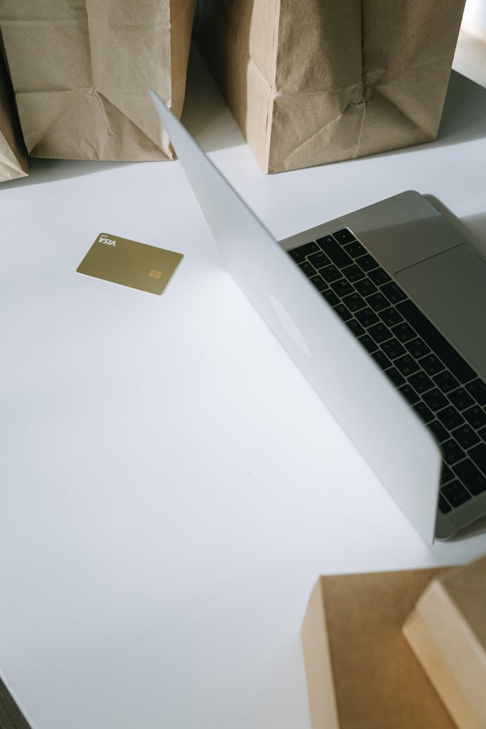 A laptop with a credit card, surrounded by paper bags, illustrating online shopping.